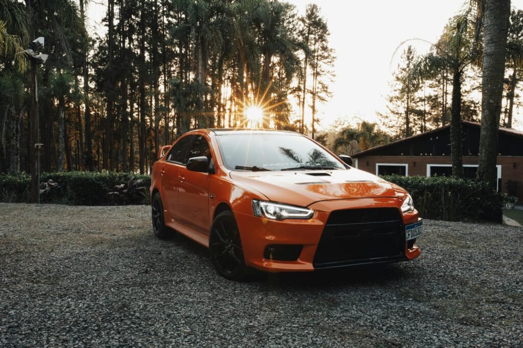 pexels-photo-24017308-24017308 An orange sports car parked on gravel with a scenic rural background at sunset, capturing natural beauty.