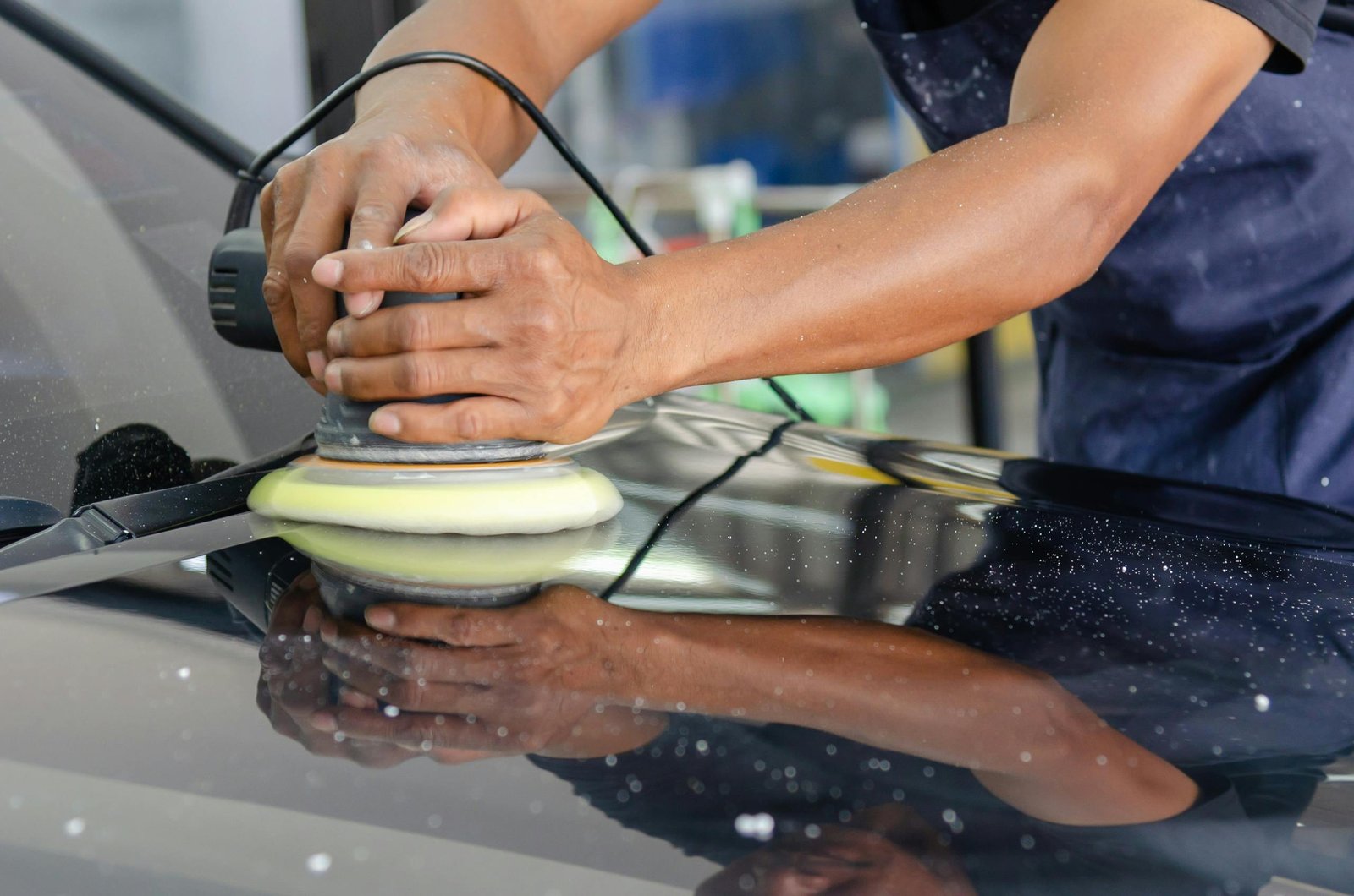 pexels-photo-5233261-5233261 Detailed view of a worker's hands polishing a car's hood using a buffer in an auto workshop.